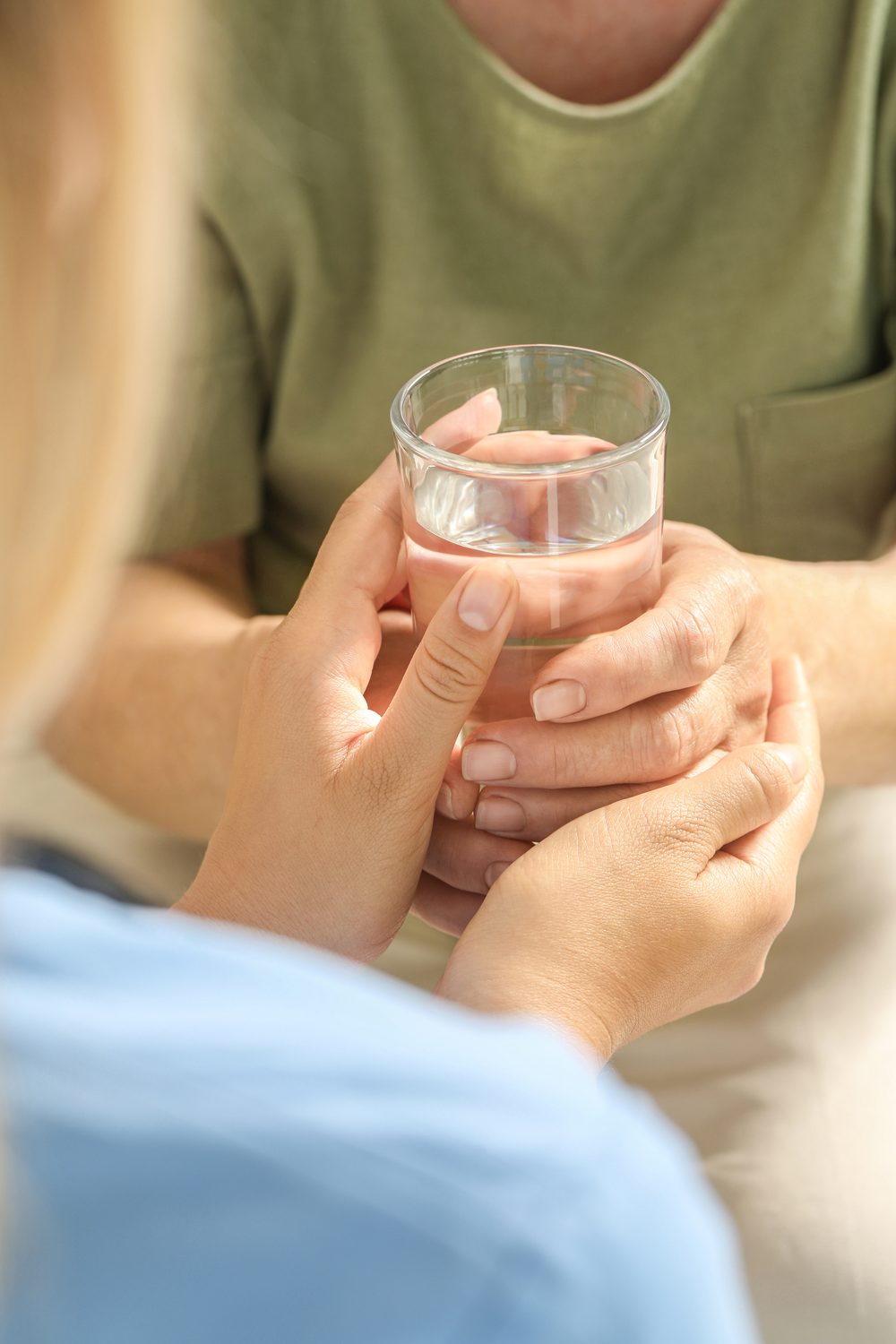 Pflegekraft reicht einer älteren Person ein Glas Wasser