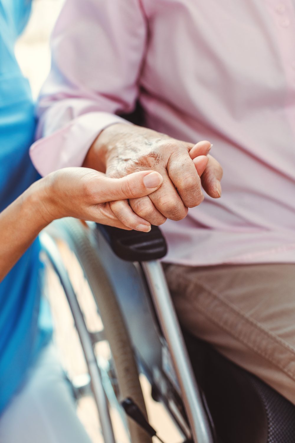 Pflegekraft hält die Hand einer älteren Person im Rollstuhl